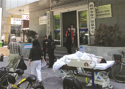 移动病床推着大妈来到房产交易中心门前