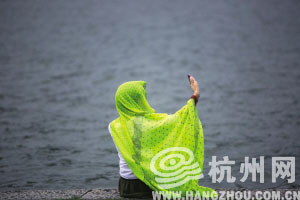 昨天下午，一个身披纱巾的游客坐在西湖边自拍。 